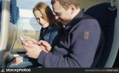 Young couple enjoying train traveling. Together they using tablet computer, laughing and having a good time