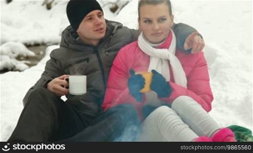 Young couple enjoying winter vacation near campfire in snowy forest