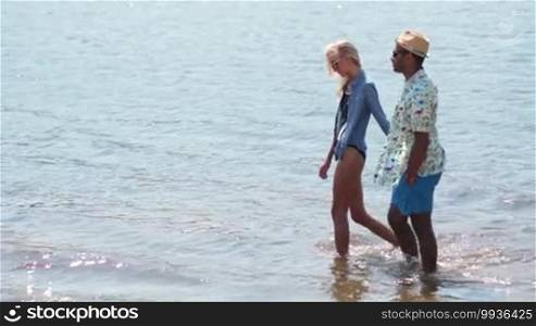 Young couple holding hands walking romantically at the water's edge on the beach during a vacation.