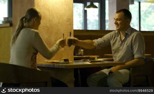 Young couple in a cafe clanging glasses, then having dinner and talking.