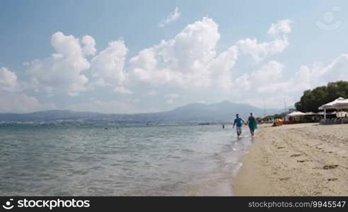 Young couple running along a beach hand in hand at the edge of the surf as they enjoy their summer vacation