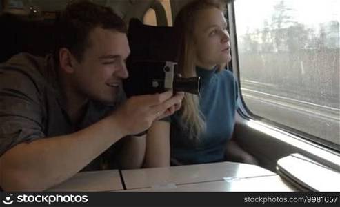 Young couple traveling by rail. Man shooting the way with retro video camera while woman looking out the window