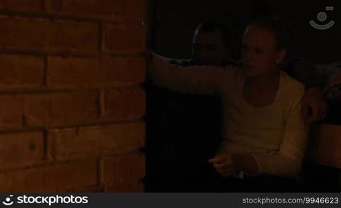 Young couple warming near stove in the evening. Woman opening the door and putting firewood into stove. Romantic atmosphere.