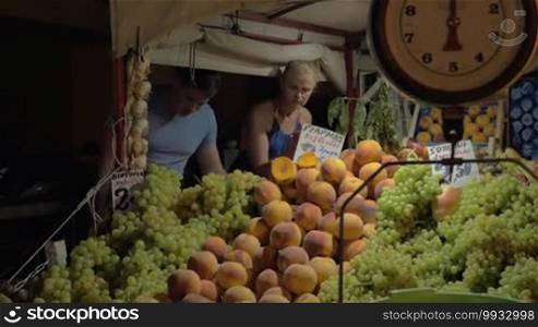 Young family couple shopping for fruit and vegetables in the evening. They selecting tomatoes on street market, fruit and scales in foreground