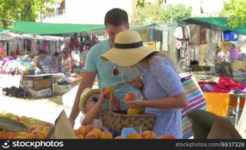 Young family - father, mother and son in market of Thessaloniki, Greece choose peaches and put them in the basket