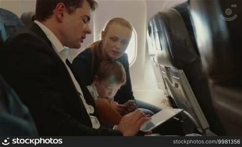 Young family of three traveling by air. Father busy with touchpad and talking to the wife, child using smartphone