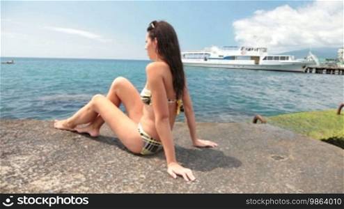 Young girl in a bikini sunbathing on the pier. In the background, a white ship at the pier.