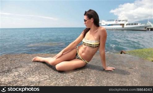 Young girl in a bikini sunbathing on the pier. In the background, a white ship at the pier.