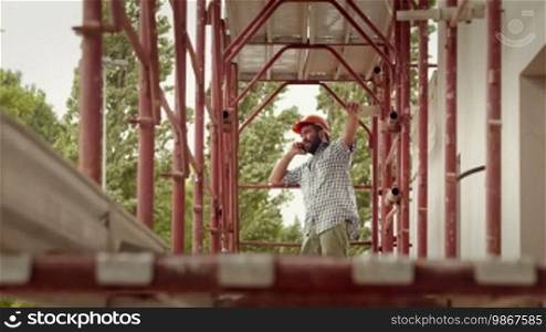 Young Hispanic man working in construction site, portrait of architect with helmet talking on mobile phone and laughing. Part 3 of 11