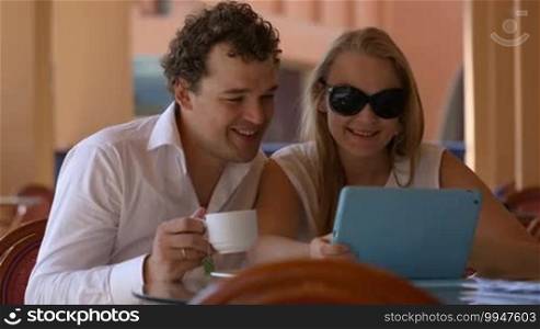 Young loving couple in cafe having tea and watching something on the tablet PC