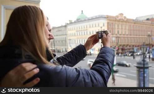 Young loving couple outdoors using a smartphone to take funny pictures of themselves. City view in the background