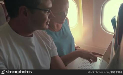 Young man and woman busy with work during the flight. Man talking and showing what to do, woman making corrections while working with laptop