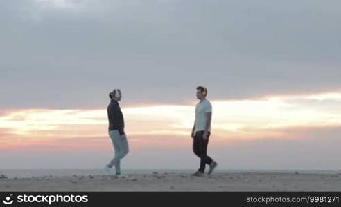 Young man and woman in wireless headphones doing physical exercises on the beach at sunset