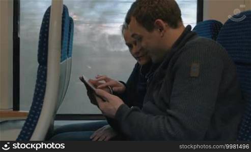 Young man and woman traveling by train. They are discussing something shown on a tablet computer. Work and entertainment with a tablet during the journey