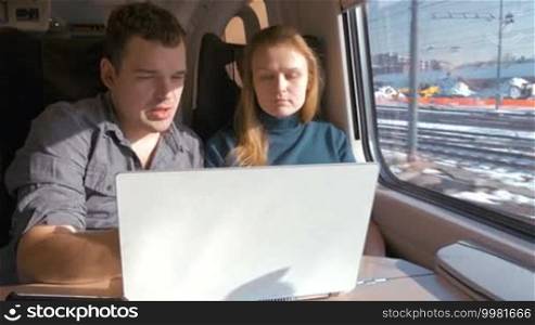 Young man and woman traveling by train. They discussing some work issue looking at laptop