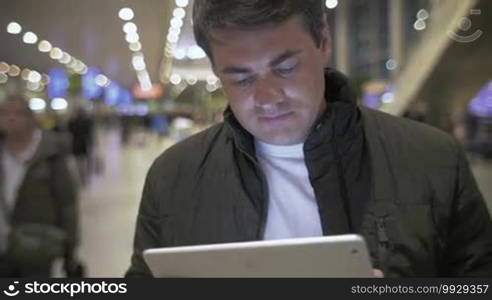 Young man in jacket using a tablet computer at the crowded airport. Easy work with a portable device