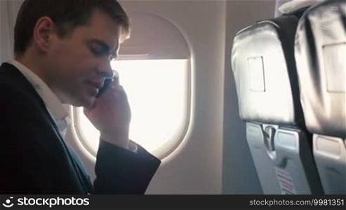 Young man on a business trip. He is traveling by plane and talking on the phone while sitting by the window.
