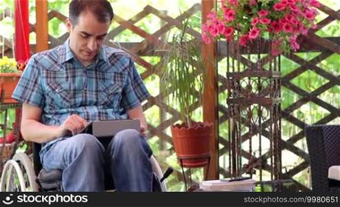 Young man on wheelchair using a tablet computer outdoors