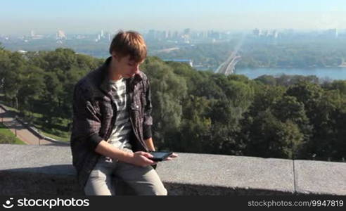 Young man reads electronic book, on background nice view of capital city, Kiev Ukraine