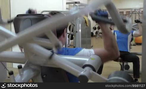 Young man using shoulder press machine in the gym with his reflection in the mirror. Hard workouts keep him fit and healthy