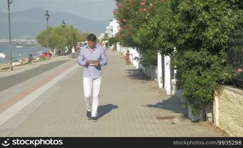 Young man with pad walking on waterfront and leaping with joy as getting good news. Businessman happy with success