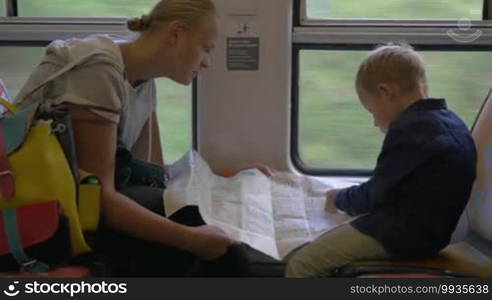 Young mother and son searching something together on map while traveling by train