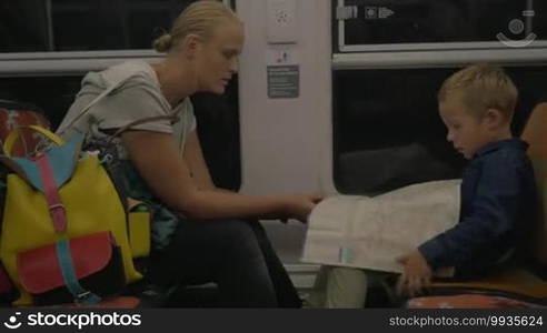 Young mother and son traveling by train. They are unfolding the map and looking at it