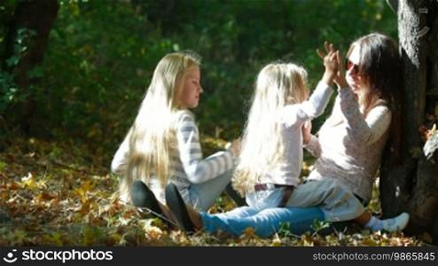 Young mother and two daughters enjoying a sunny day in the park, talking and laughing. Long shot
