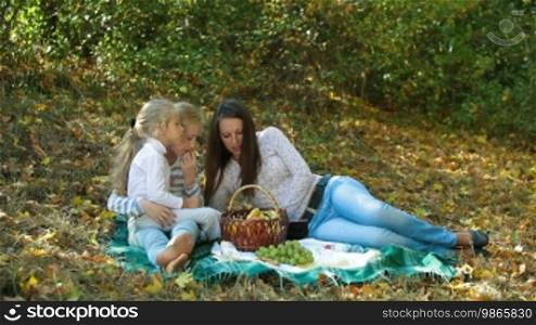 Young mother and two daughters having a picnic in the autumn park, reading a book