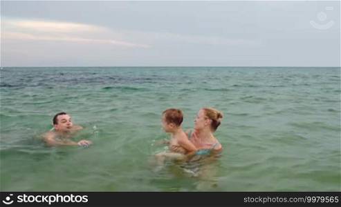 Young parents playing ball with little son in the sea. Family fun during summer vacation