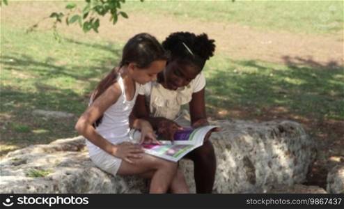 Young people and education, two little girls reading a book in the city park