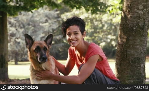 Young people and pets: Portrait of a happy Hispanic girl at work as a dog sitter with an Alsatian dog in the park