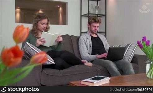 Young people at home, man and woman lifestyle, boyfriend and girlfriend relaxing, happy college students studying for school homework with book and notebook computer, laptop pc. Education and friends