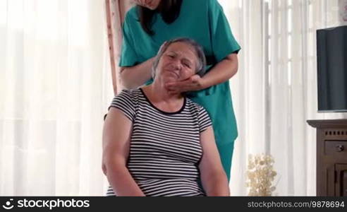 Young physiotherapist nurse giving head massage to senior woman at home or in a nursing home. Slow motion handheld movement