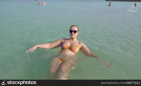 Young pregnant woman swimming on the back in salt water of Dead Sea. Recreation on resort in Israel