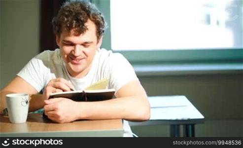Young smiling man at home taking notes and drinking tea