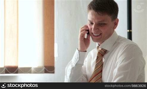 Young smiling man talking on a cell phone in the living room