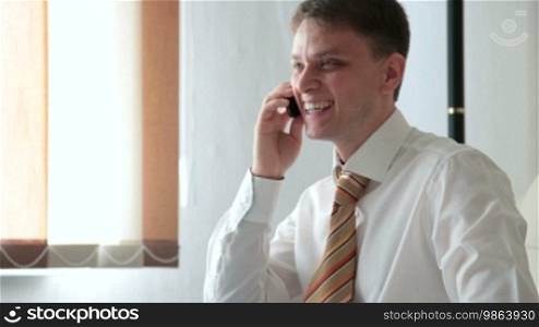 Young smiling man talking on a cell phone in the living room