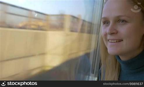 Young smiling woman enjoying looking out the window in train. Traveling by train can show many interesting and beautiful places
