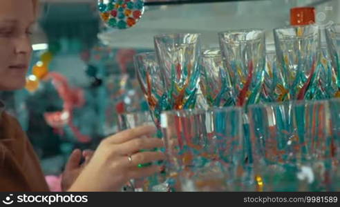 Young smiling woman in the store looking at beautiful Venetian glass, taking one small cup and leaving