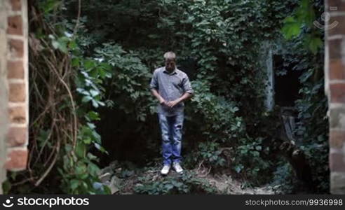 Young street style dancer dressed in urban style dancing in abandoned building. Man dancing street dance over green trees and plants background