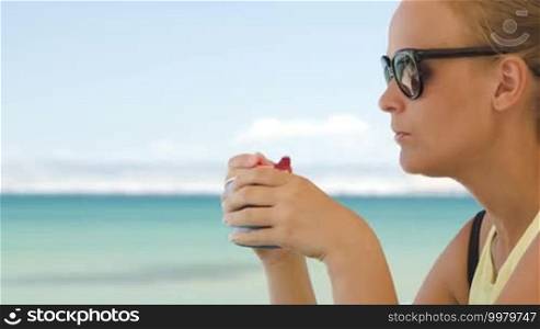 Young woman eating ice cream on the beach on a hot summer day. Bright blue sea and sky in background