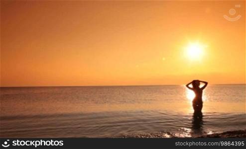 Young woman in a bikini at sunset coming out of the sea