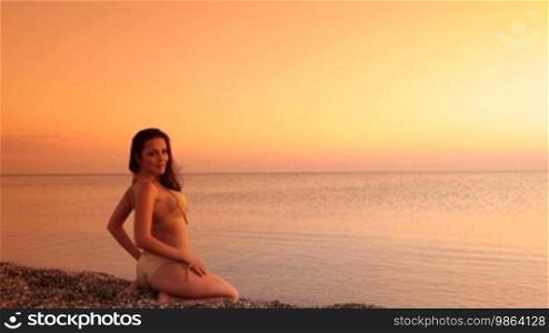Young woman in bikini sitting on beach at sunset