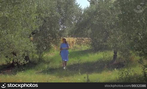 Young woman in summer hat walking outdoor on sunny day and using tablet computer to take nature shots