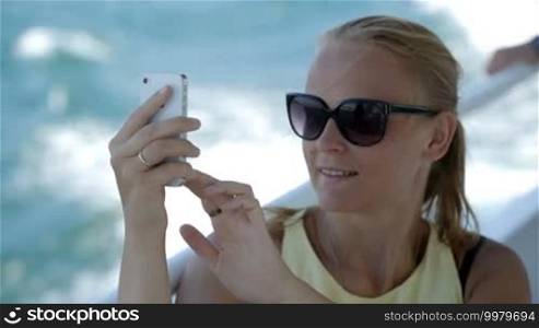 Young woman in sunglasses making selfie using smartphone while traveling by boat