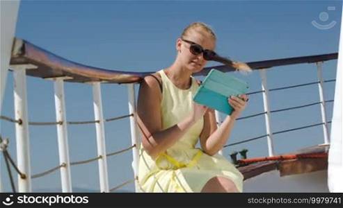 Young woman in sunglasses using tablet computer while traveling by ship on a windy day