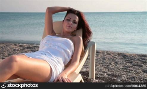 Young woman in white short dress resting by the sea