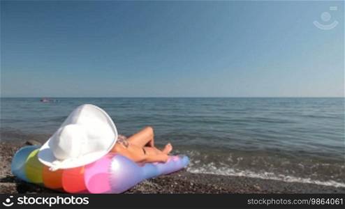 Young woman in white sun hat tanning on beach