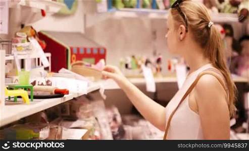Young woman is choosing toys for her kid in the toy store in the supermarket